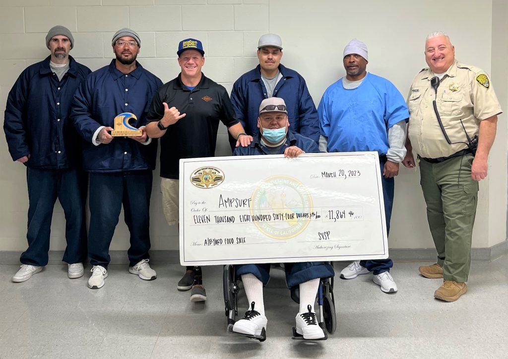 Incarcerated men and correctional officer present an oversized check to Dana Cummings.