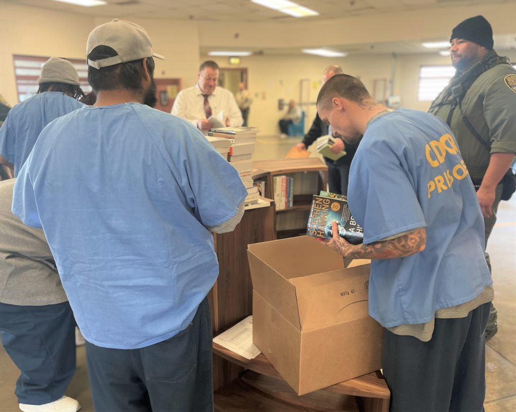 A group of incarcerated people and staff unbox books and put them on bookcases.