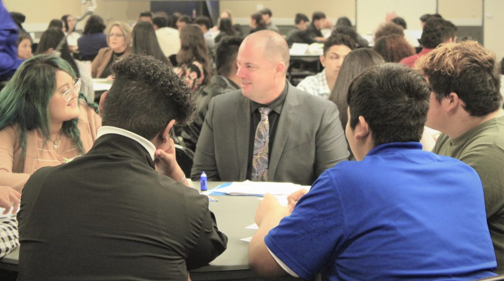 Valley State Prison (VSP) acting warden mentors high school students at a table during Junior Ethics Day.