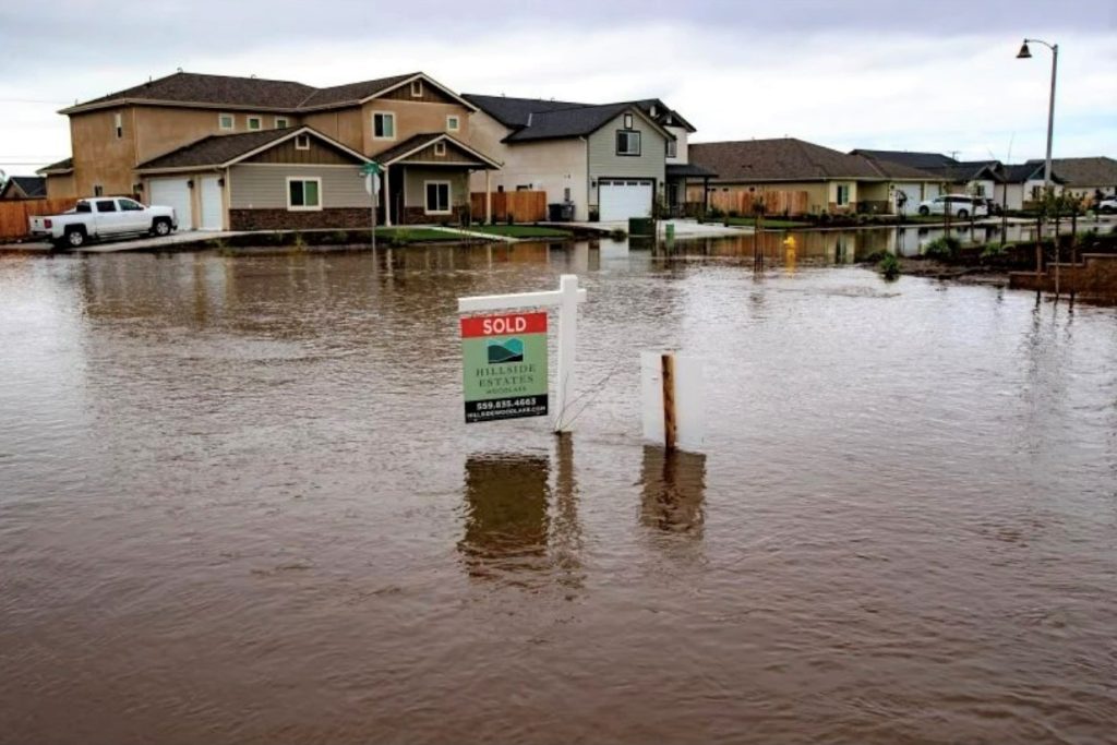 A real estate sign on a flooded street . The sign is mostly underwater.