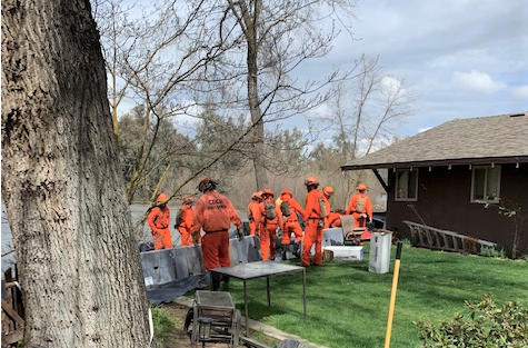 About 10 people in orange jumpsuits build a retaining wall outside a brown house.
