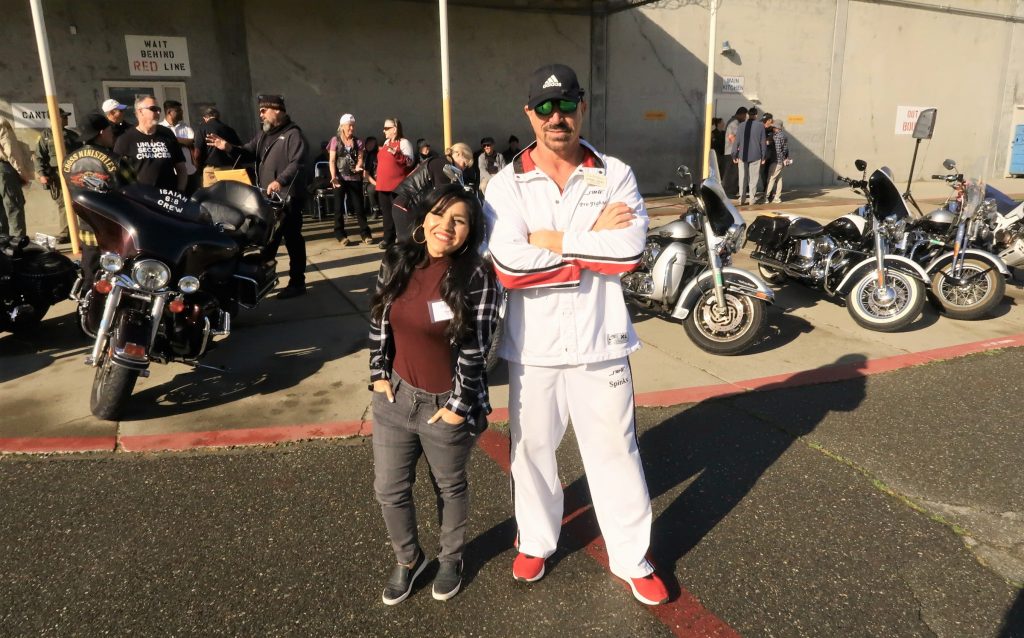 A singer and a martial arts expert standing in front of motorcycles at a prison.