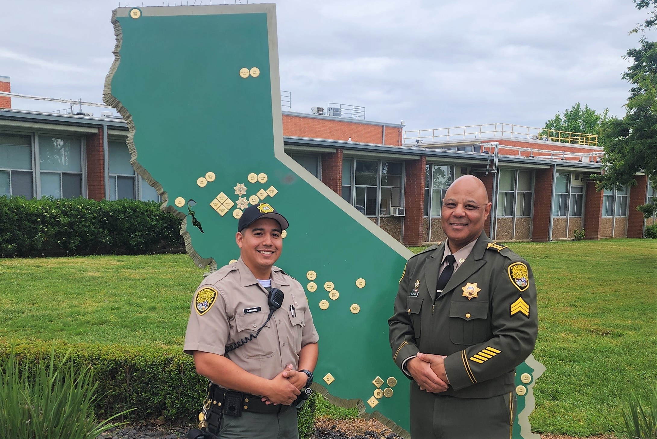 A training sergeant and cadet stand in front of a California map and a school building use to train correctional officers.