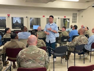 man stands while people sit around him at CMF military assistance program