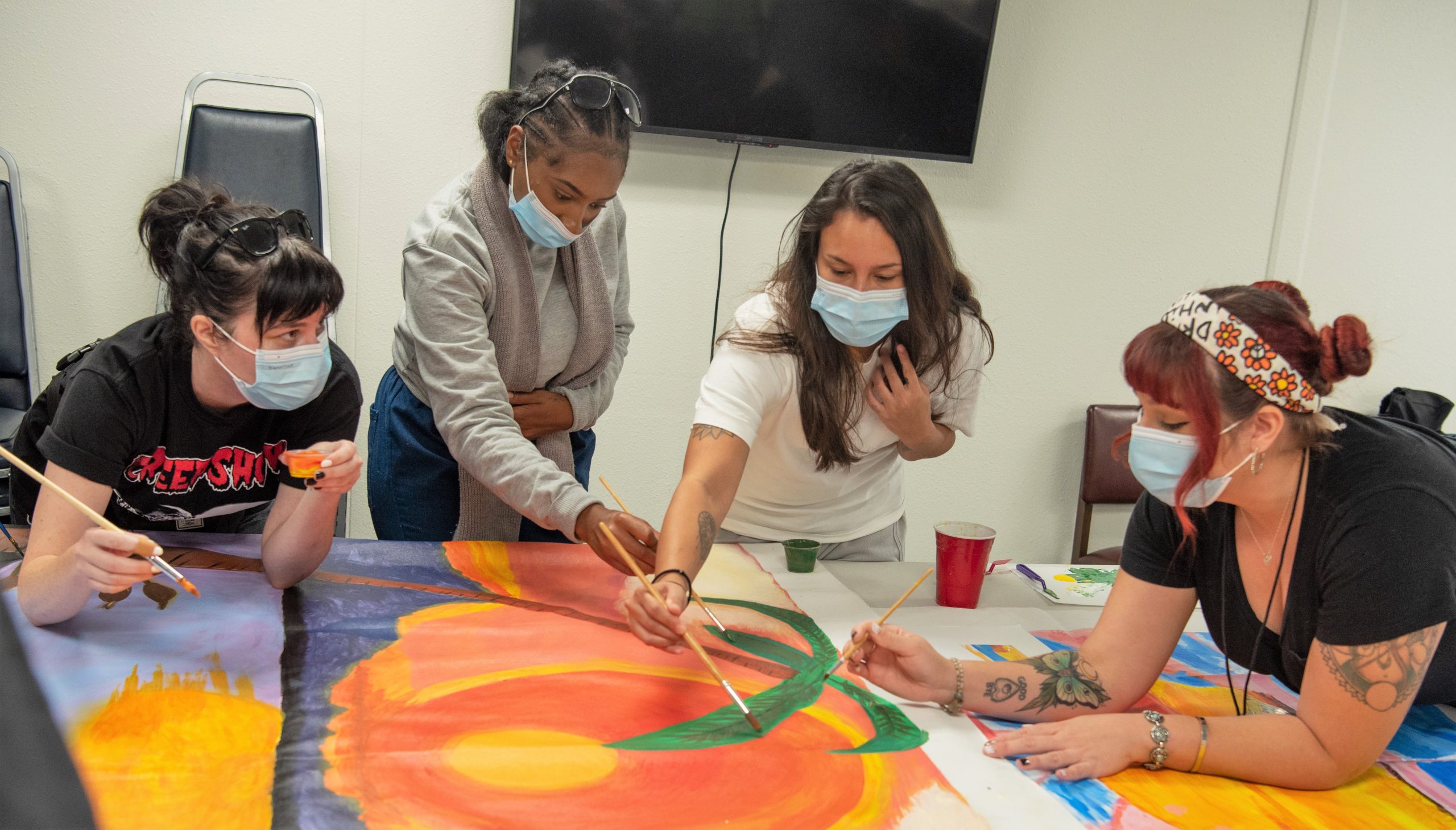 Two art teachers and two incarcerated women at a prison working on a painting.