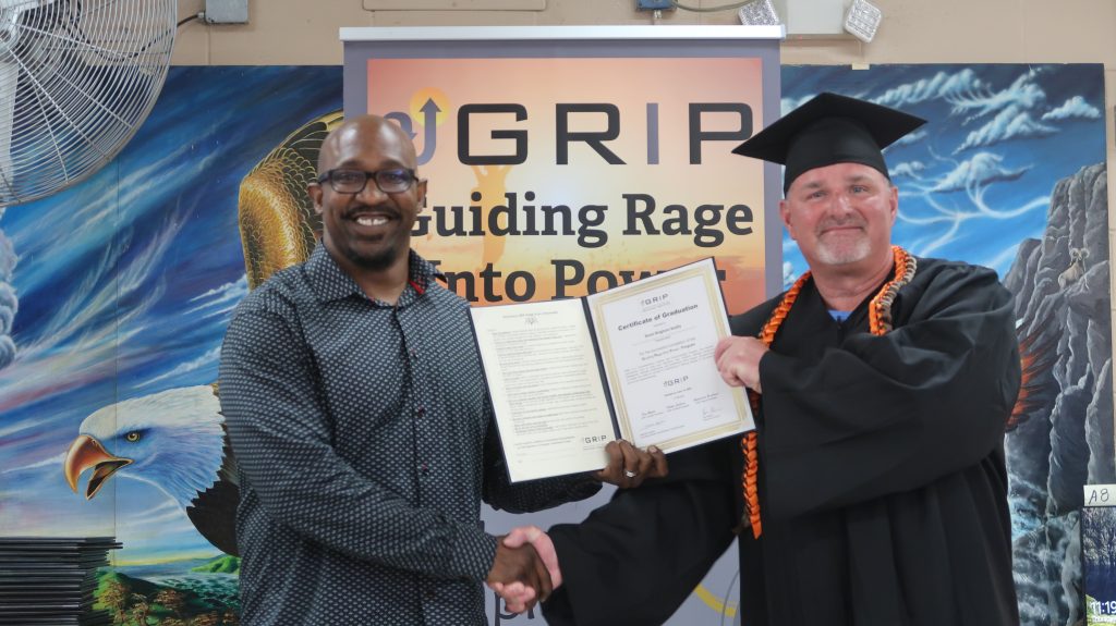 Man shakes hands with a GRIP graduate while holding a certificate.