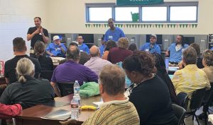 Incarcerated students sit along one side of the wall while visiting college professors ask questions about correctional education.