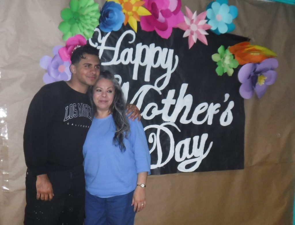 Mother's Day photo backdrop created by staff with incarcerated mom an son standing in front of it.