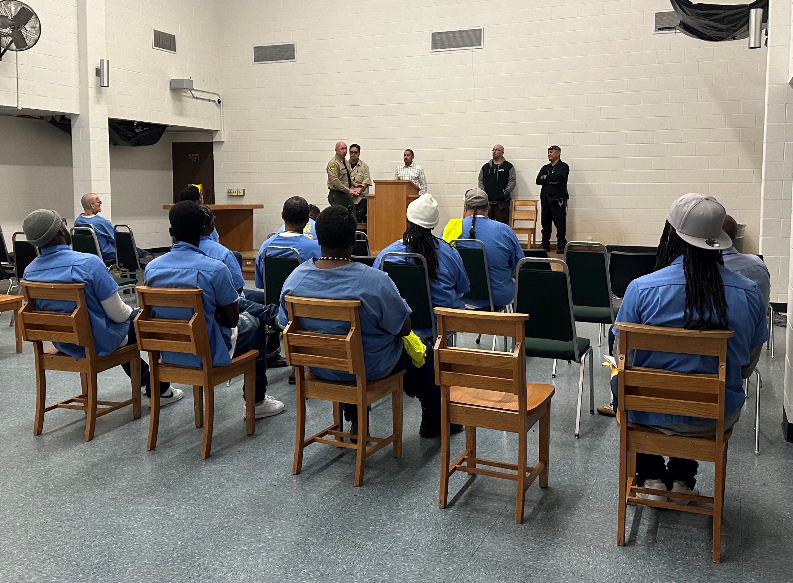 Incarcerated people sit in front of a stage as they listen to parole agents and two formerly incarcerated people.
