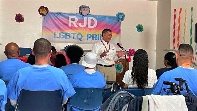 Man speaks to incarcerated people while a banner behind him reads: "RJD LGBTQ Pride."
