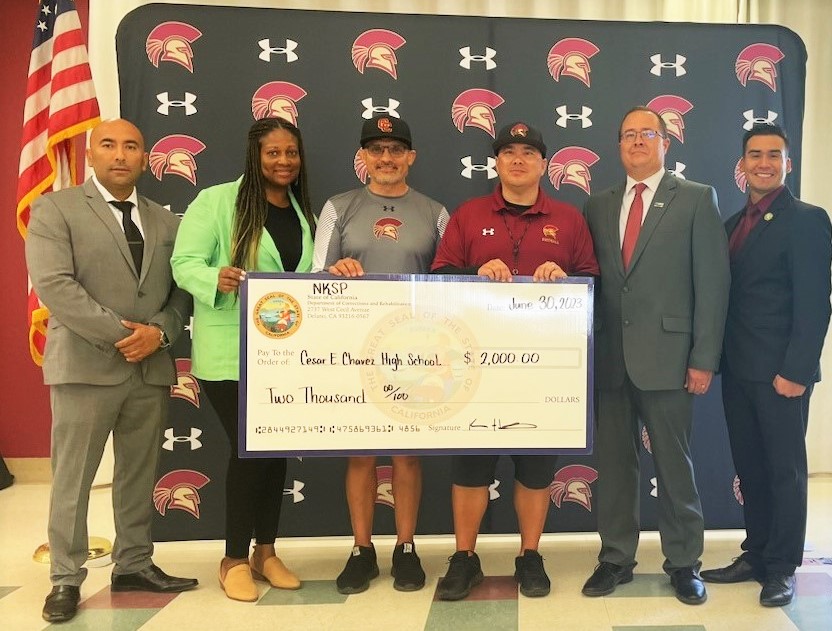 Prison leaders and high school football coaches hold an oversized check.