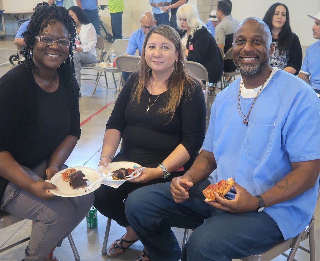 incarcerated sitting with two visitors enjoying pizza and cake at VSP HART Graduation