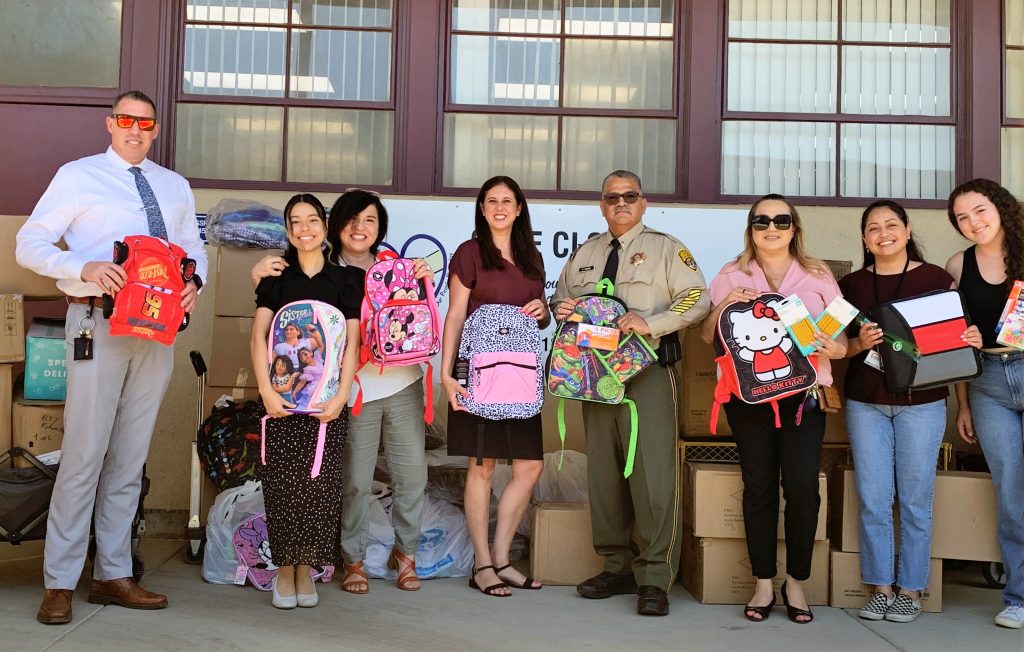 CIM staff and school workers hold backpacks and other school supplies.