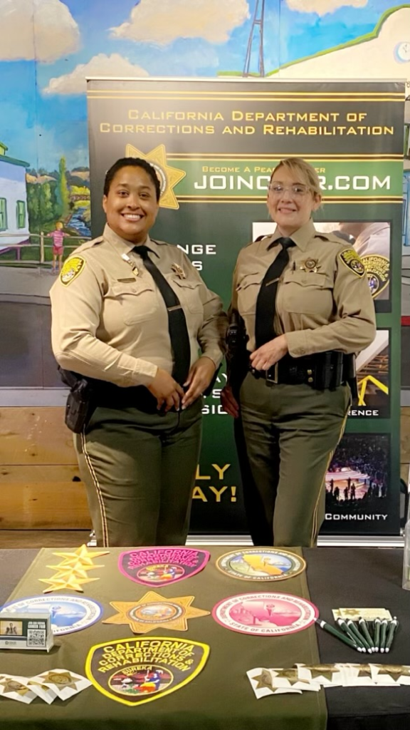 two correctional officers standing at recruitment table