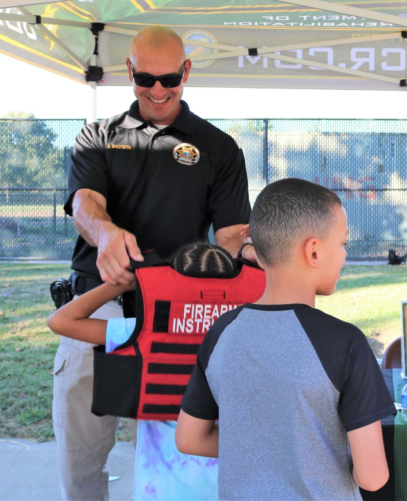 A CDCR sergeant puts a vest on a child during National Night Out.
