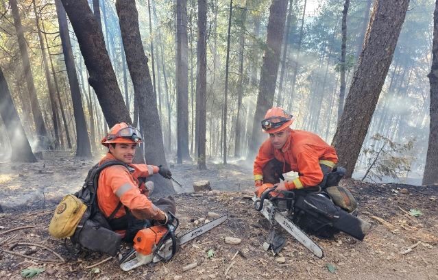 Two PGYCC firefighters sit beside smoldering forest in Nevada County.