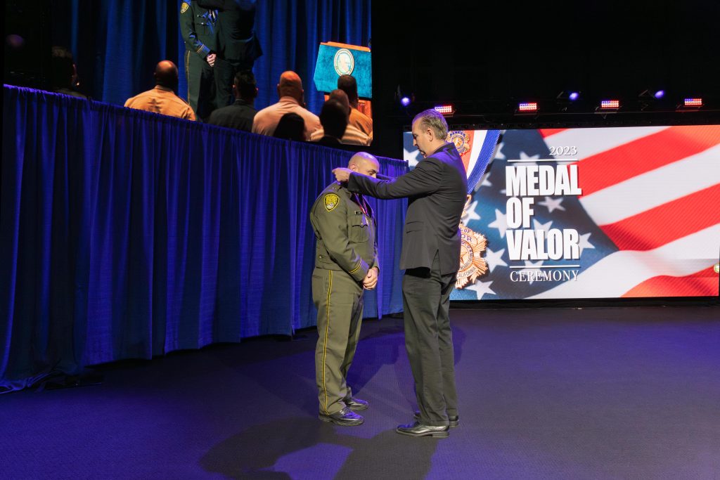 CDCR secretary hangs a medal around the neck of Lt. Faria while both men stand on a stage.