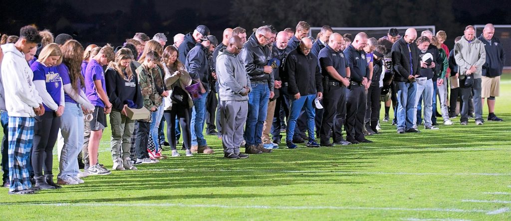 People with heads bowed stand on a football field.