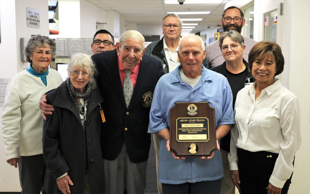 An incarcerated person holds an award while posing for a photo with people from the Lions Club and staff members.