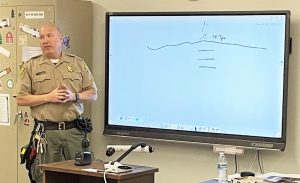 Education correctional officer mortell stands at a white board while incarcerated people sit in a classroom.