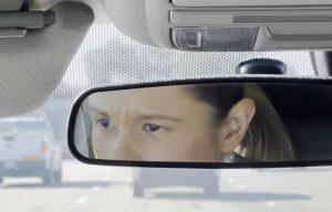 A Day in the Life of Parole Agent Vivian Miramontes. She's driving on the highway and her image is seen in the rearview mirror.