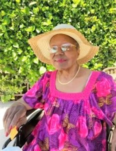 Ethel Anthony wearing a sunhat and brightly colored dress with greenery in the background.