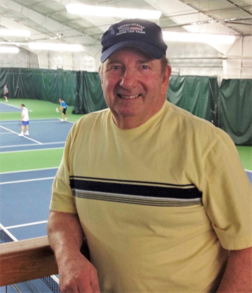 Dennis Burgi stands in an area with tennis playing in the background.
