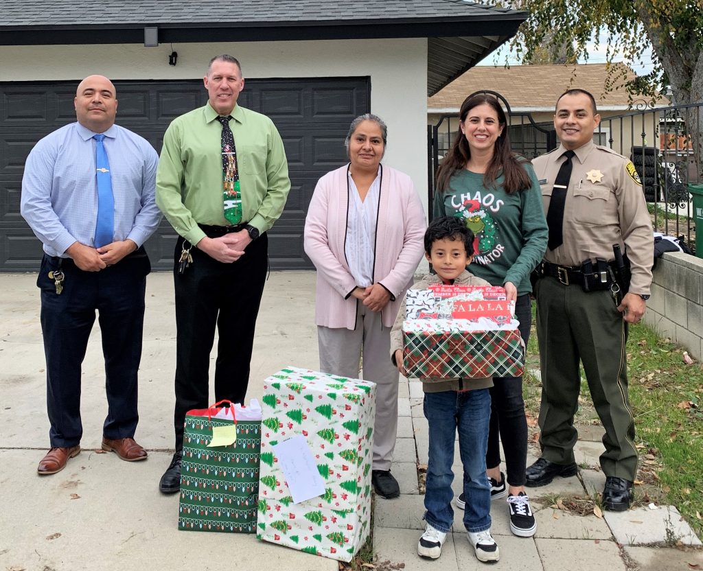A family receives gifts from California Institution for Men staff. They are all standing in front of a house.