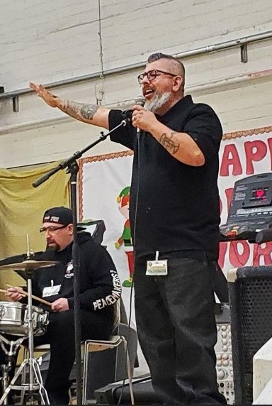 A man plays drums in the background while another man holds a microphone.