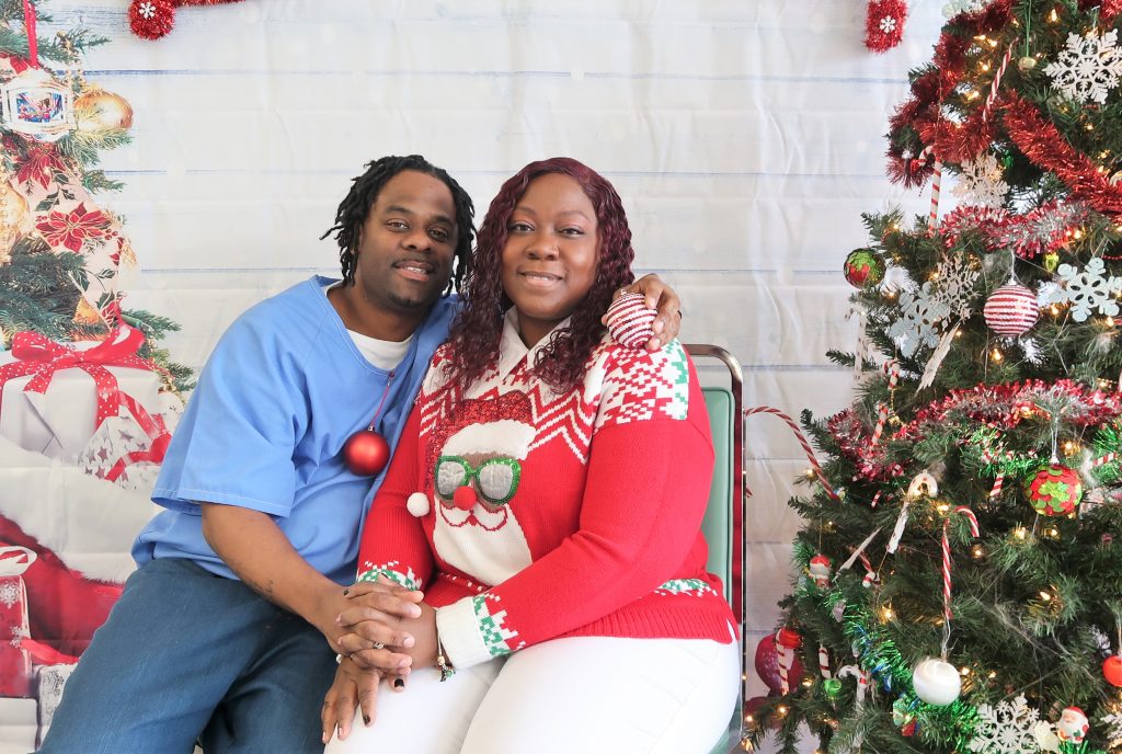 Holiday visiting at a prison with a man and woman sitting beside a Christmas tree.