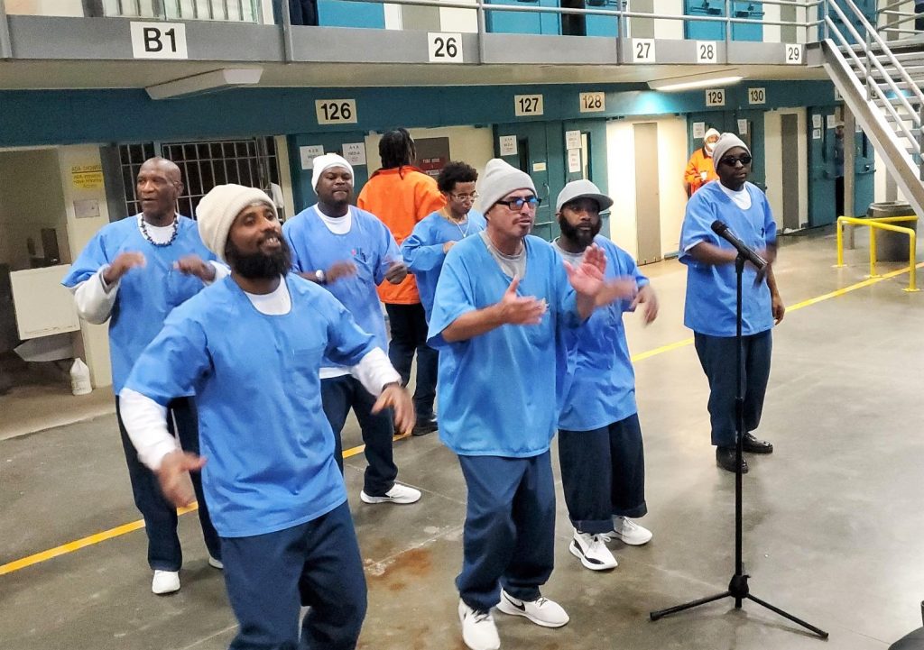 Incarcerated people sing into microphones.