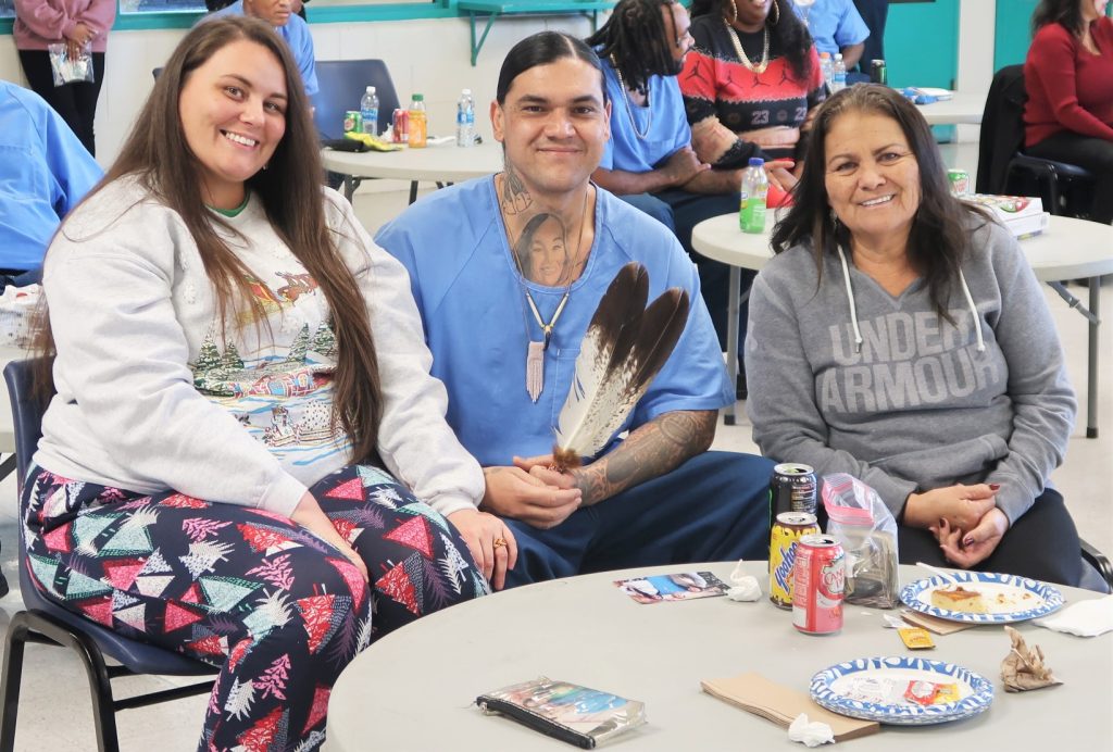 Two women and an incarcerated person holding two feathers.