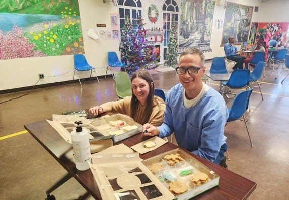 Two people decorate cookies in a prison visiting room.