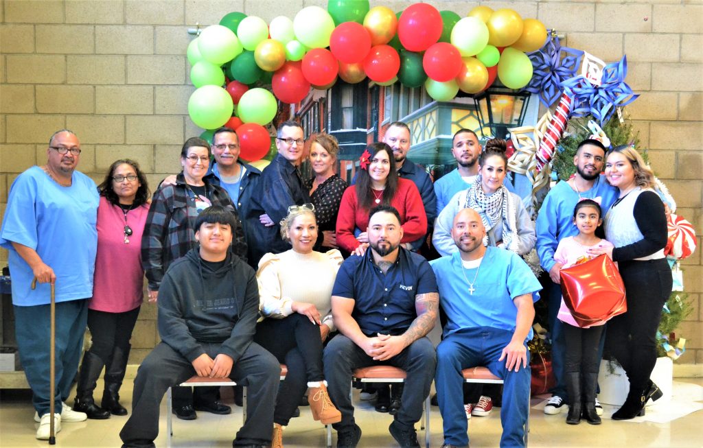 Incarcerated people and their families sit under a colorful archway decorated for the holidays.