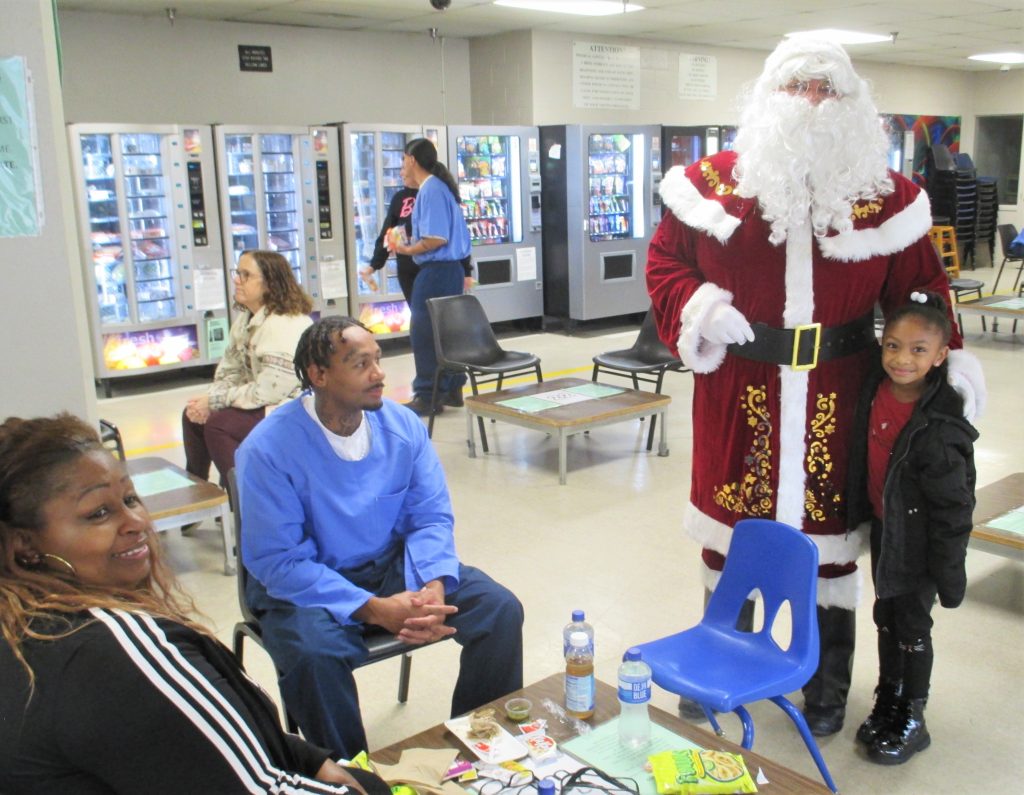 A prison visiting room with incarcerated people and their families with Santa.