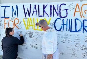 A banner with the words "I'm walking for Valley Children's Hospital" while a Corcoran prison warden and incarcerated person sign the banner.