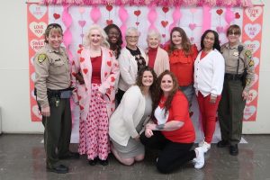 Valentine's visiting event photo shows the inmate family council with California Men's Colony Visiting staff with a Valentine's backdrop.