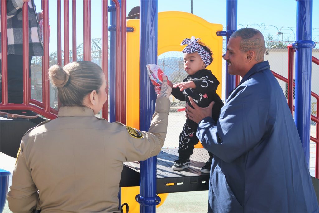A prison visiting staff member gives a Valentine's gift to a child being held by an incarcerated person.