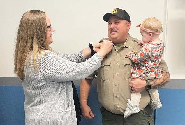 A woman pins bars on a lieutenant who is holding a baby.