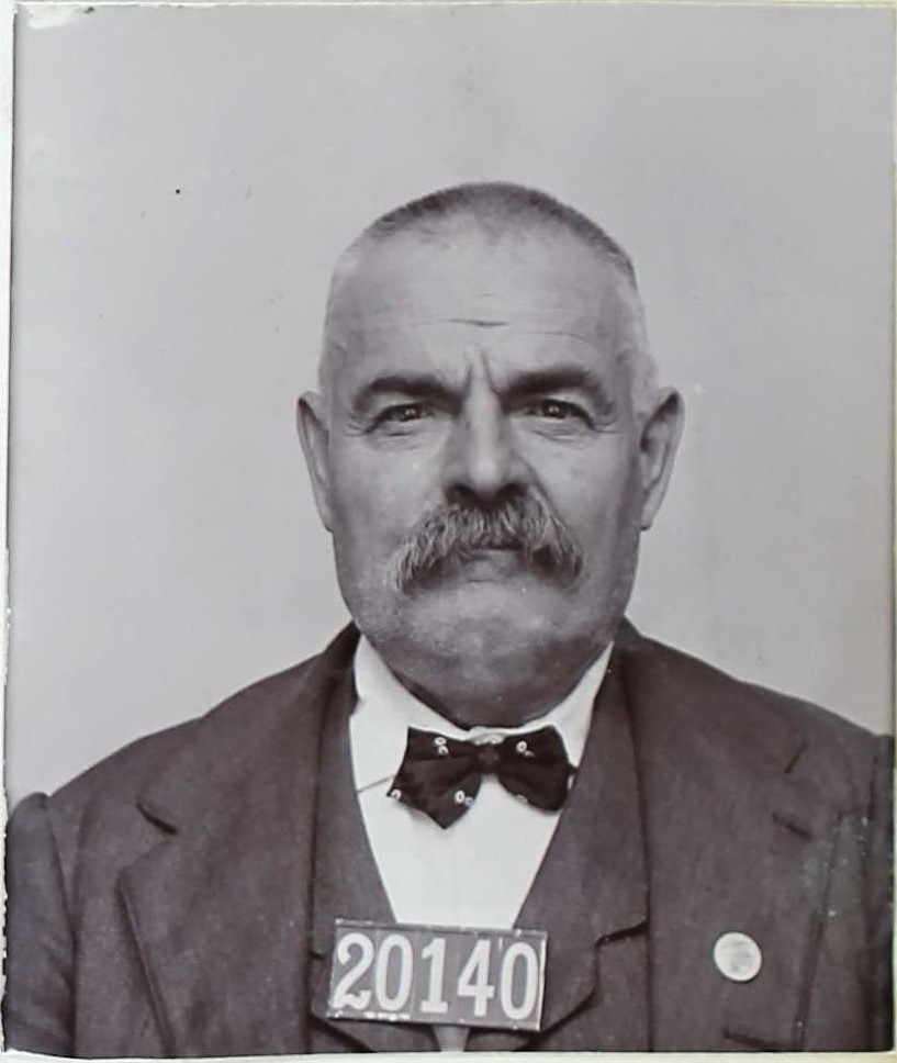Man wearing bowtie and the numbers 20140 on his chest in a booking photo.