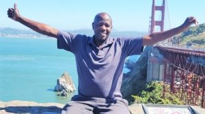 Man sits on a wall with a bridge behind him.