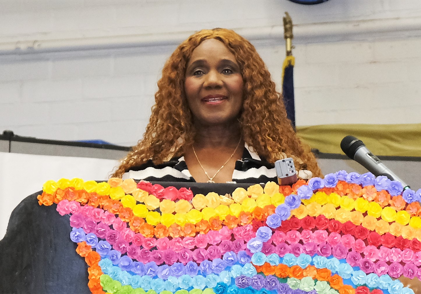 A woman with long hair stands behind a decorated lectern to speak to the incarcerated people at California Institution for Women (CIW) for Women's History Month.