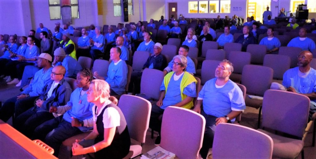 An audience of mostly incarcerated people listen to Matt Butler perform music.