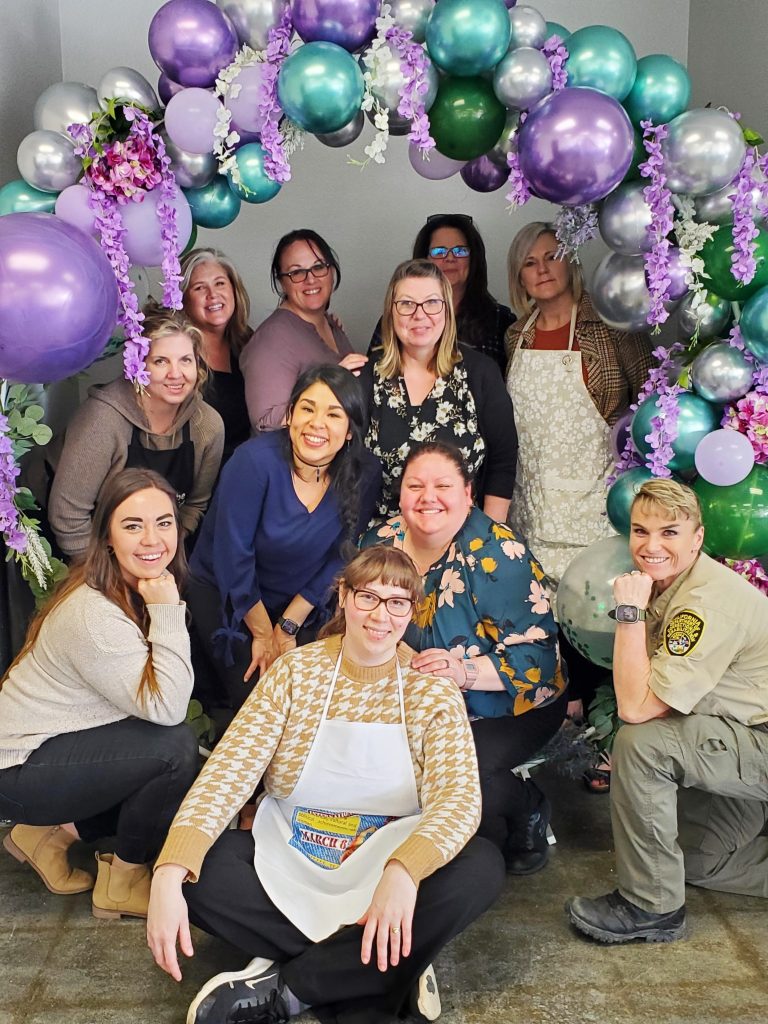 Prison staff pose under a balloon archway for a women's event.