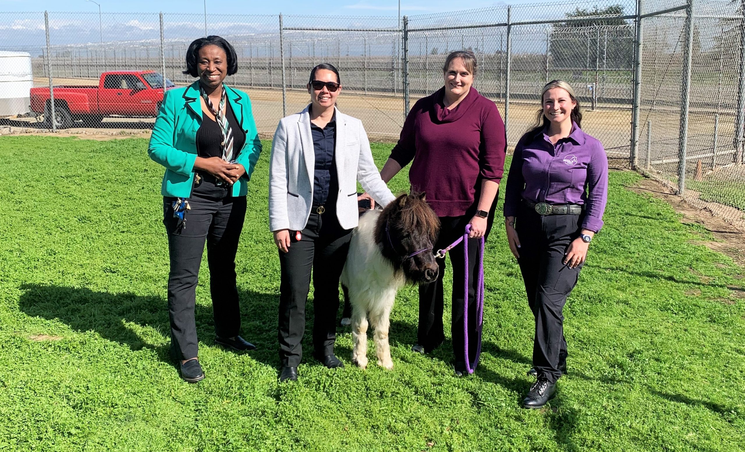Four women with a pony from Rebel Farms standing in a prison yard.