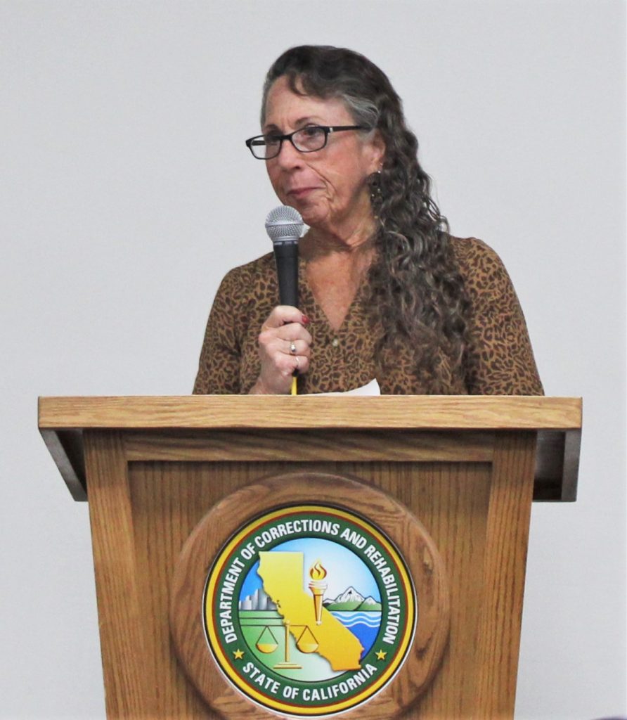 A woman holds a microphone and speaks at a crime victims event at Centinela State Prison.