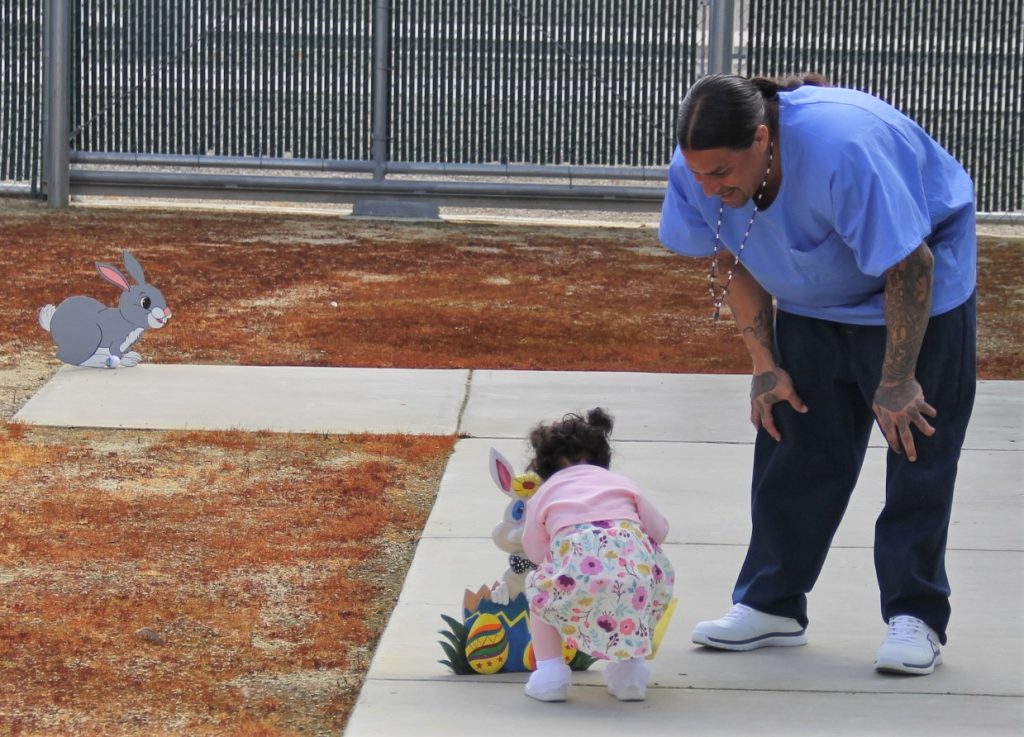 An incarcerated person helps his child hunt for Easter eggs at CHCF in Stockton.