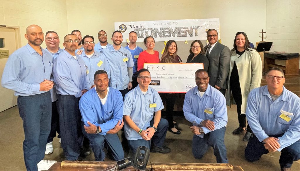 A group of people, most incarcerated, with an oversized check to donate to a charity.