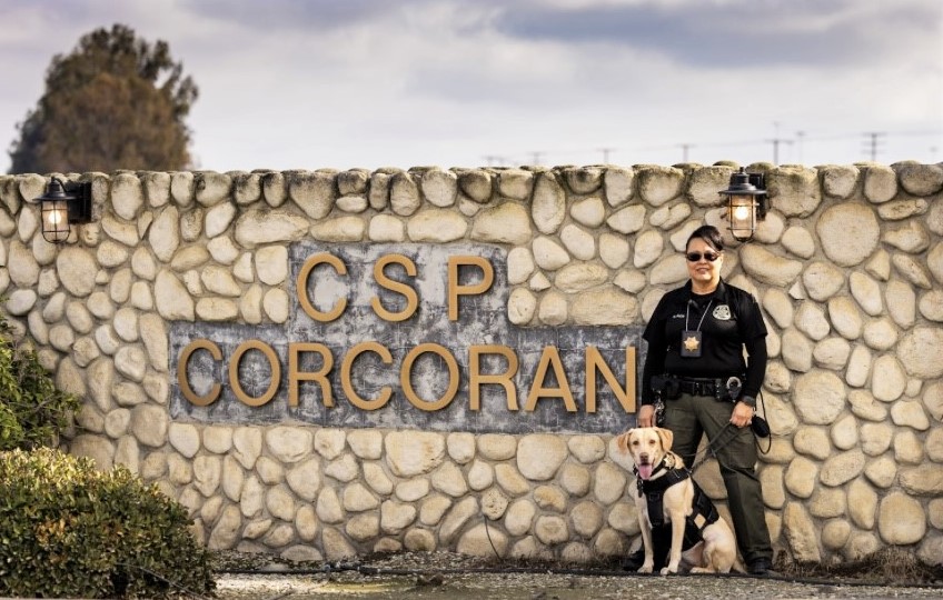 K-9 Mango with her handler, Officer Rios, at the CSP-Corcoran sign.