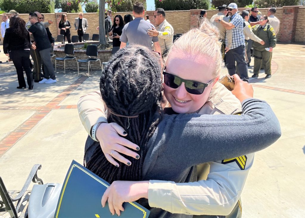 Two women, one of them in a uniform, hug during a ceremony.